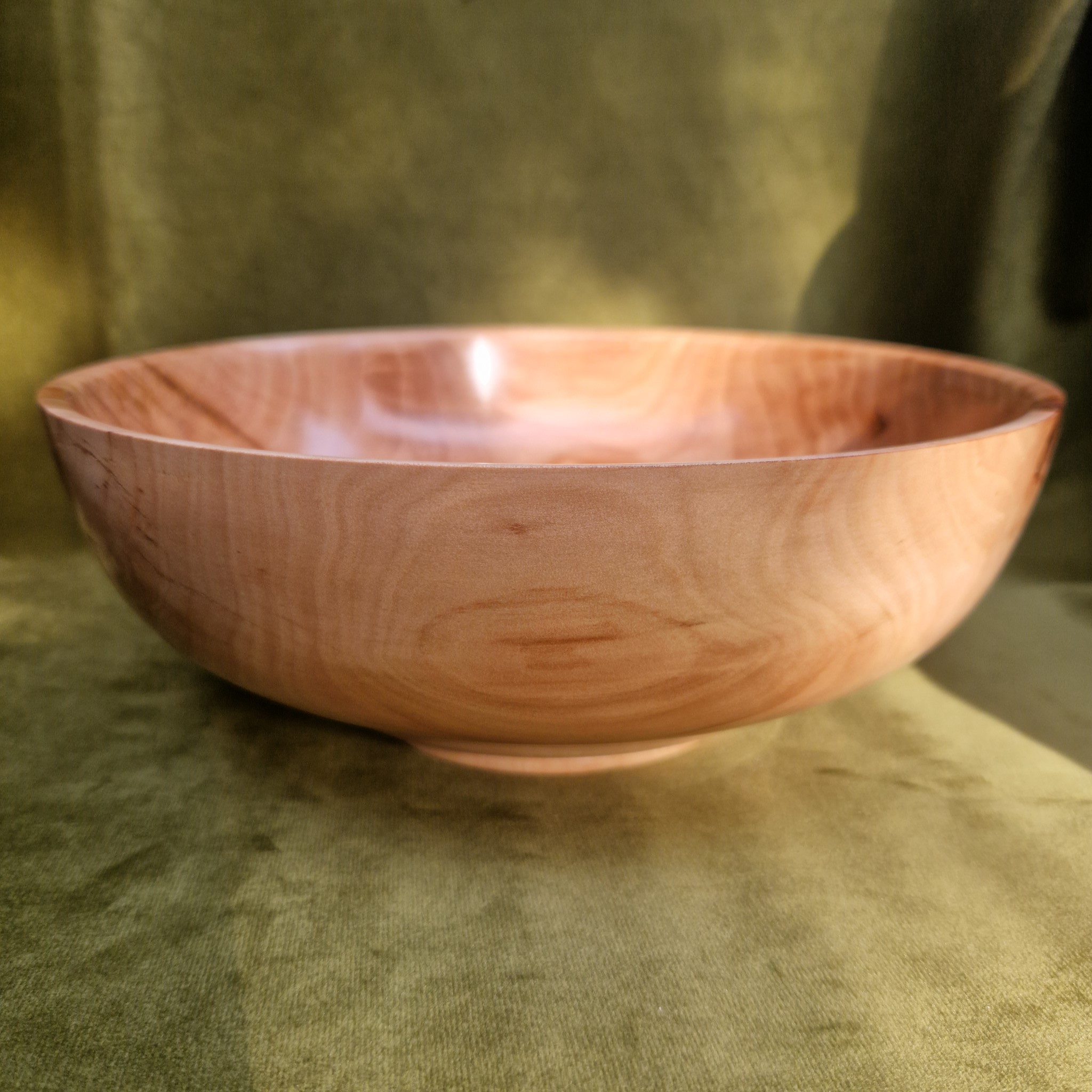 Apple wood fruit bowl on green cloth, side profile
